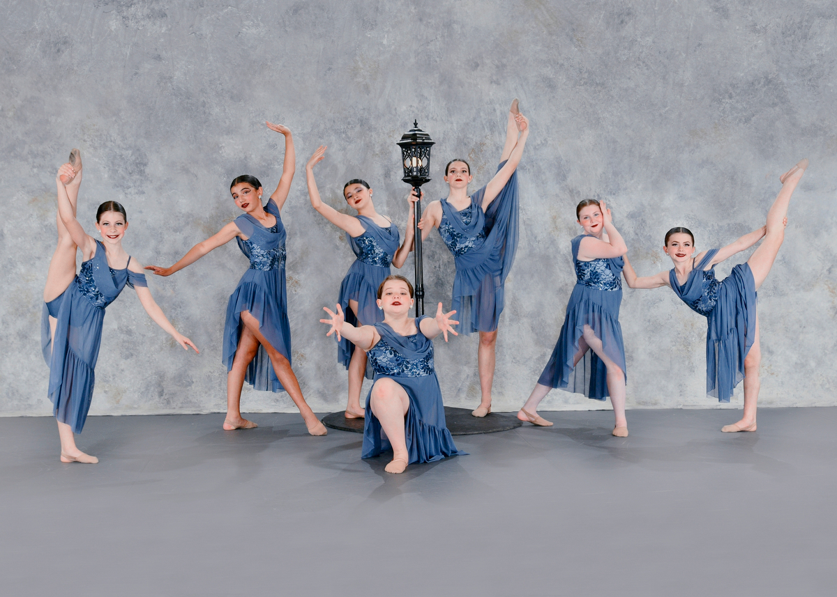 Group of seven dancers in blue dresses posing around a lamppost