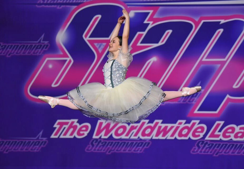 Ballerina performing a grand jeté in a white tutu at Starpower competition